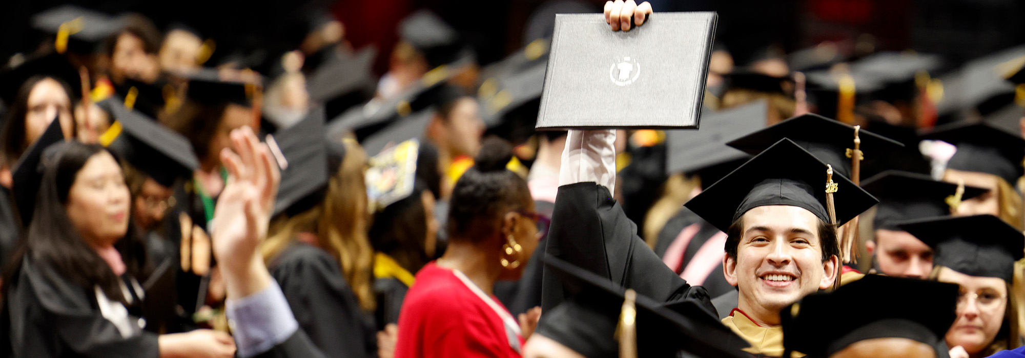 A graduate holds up their diploma cover after the ceremony among a crowd of other graduates.